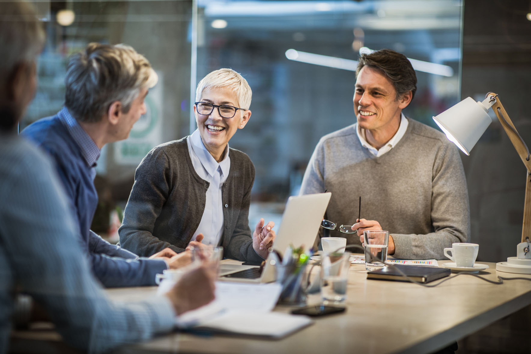 employees in meeting room talking and smiling around a laptop